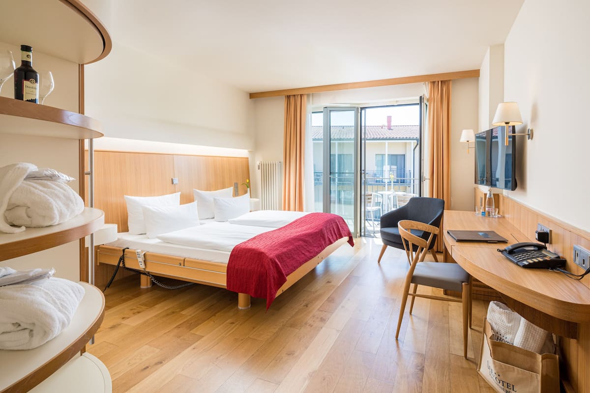 A hotel room with a bed, a desk, a chair, a TV, and a view of the outside.