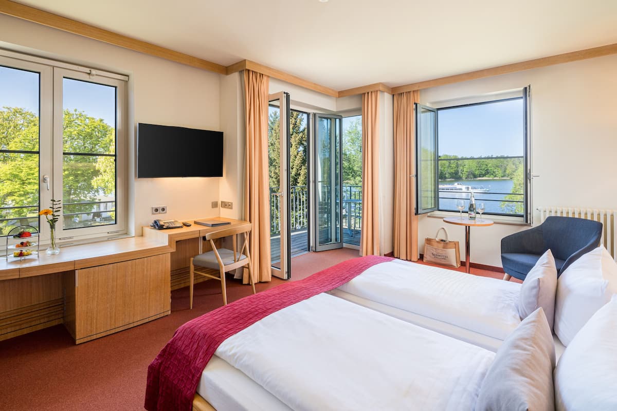 A hotel room with a bed, desk, chair, TV, and a view of a lake.