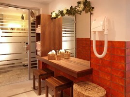 Un baño con tocador de madera, dos taburetes, un espejo, un perchero y zona de ducha.