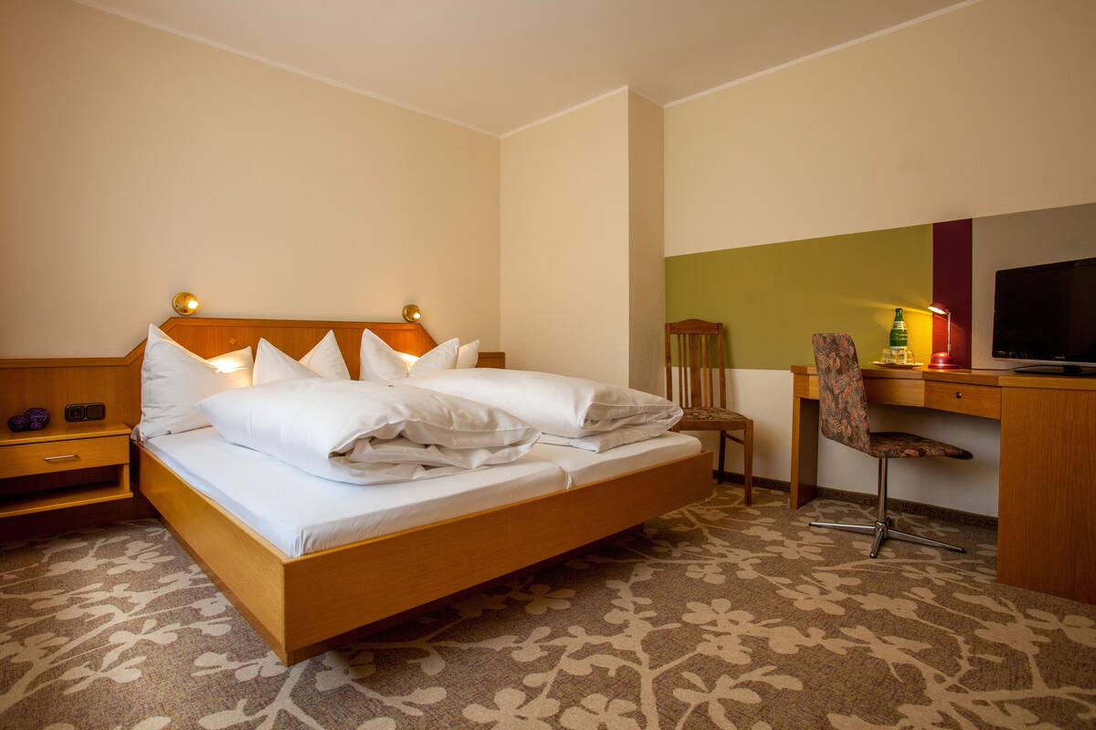 A hotel room with a bed, a desk with a chair, a television, and a nightstand.