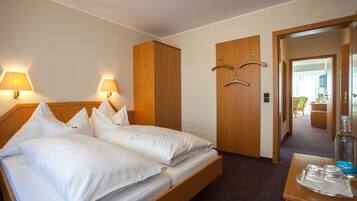 A hotel room with a double bed, two bedside lamps, a wooden wardrobe, a small table with a bottle and glasses, and a mirror.