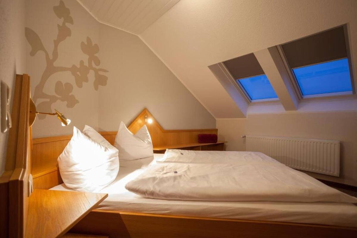 A bedroom with a sloped ceiling, a bed with white bedding, a wooden headboard, and a skylight.