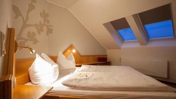 Un dormitorio con techo inclinado, cama con ropa de cama blanca, cabecero de madera y tragaluz.