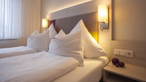 Habitación de hotel con dos camas, ropa blanca, cabecera de madera, lámparas de noche y mesita con adornos esféricos.