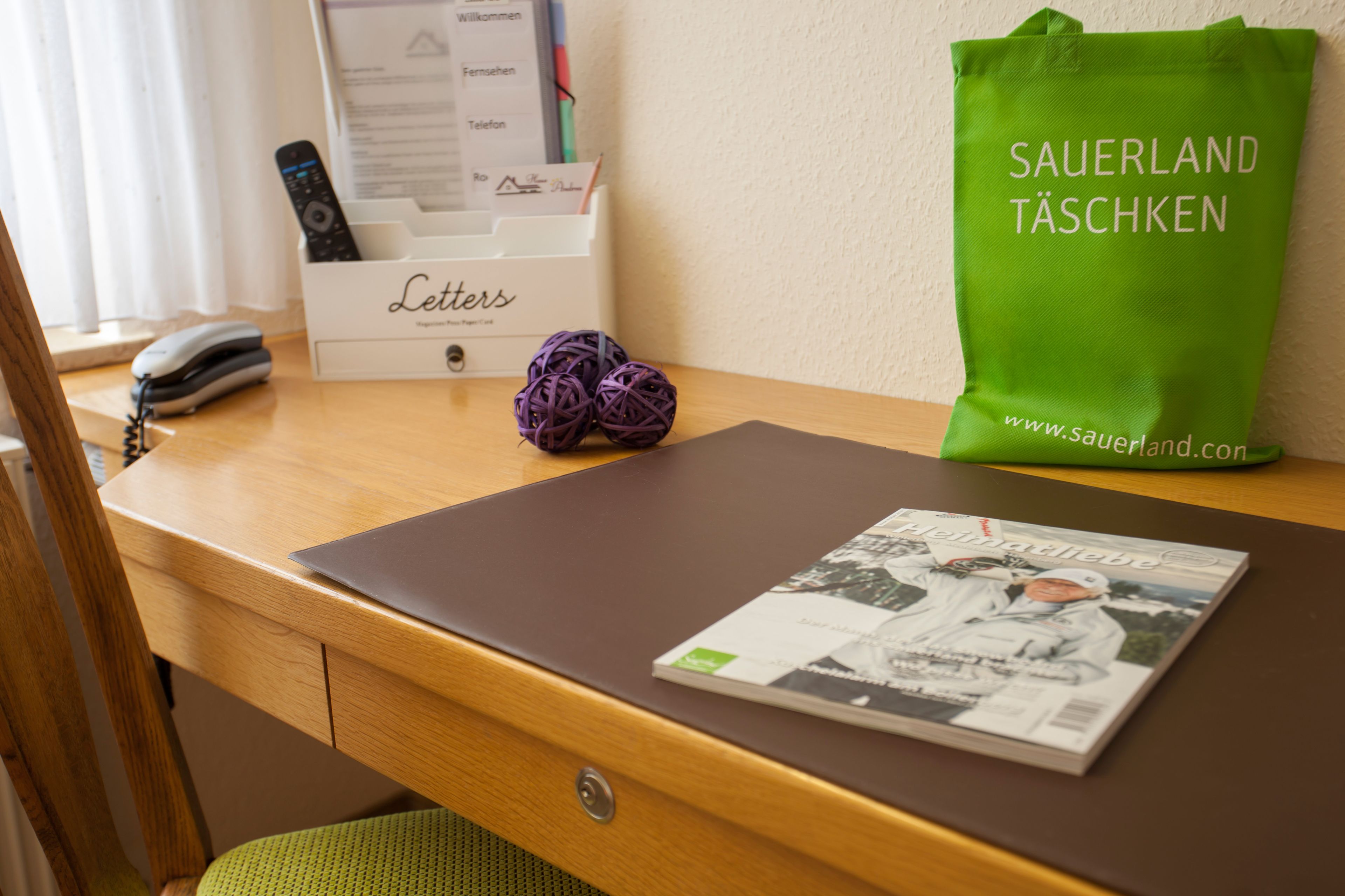 Una scrivania con un portatile, una rivista, una borsa verde e una scatola di lettere.
