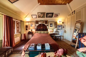 A bedroom with a large bed, a desk with books, a dresser, and a mirror.