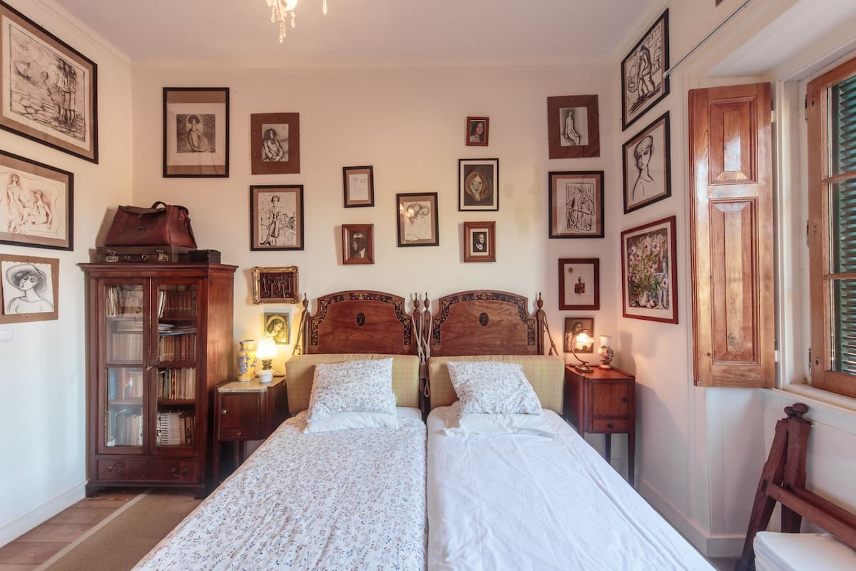 Een slaapkamer met twee bedden, een houten kast en meerdere kunstwerken in lijsten aan de muur.
