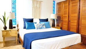 A neatly arranged bedroom with a bed, two bedside tables, a macrame wall hanging, and wooden wardrobes. - Pazifico Villas (Tamarindo)