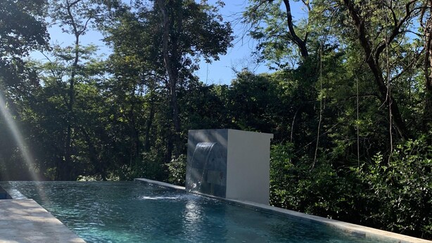 A rectangular swimming pool with clear water, surrounded by lush greenery and trees. - Pazifico Villas (Tamarindo)