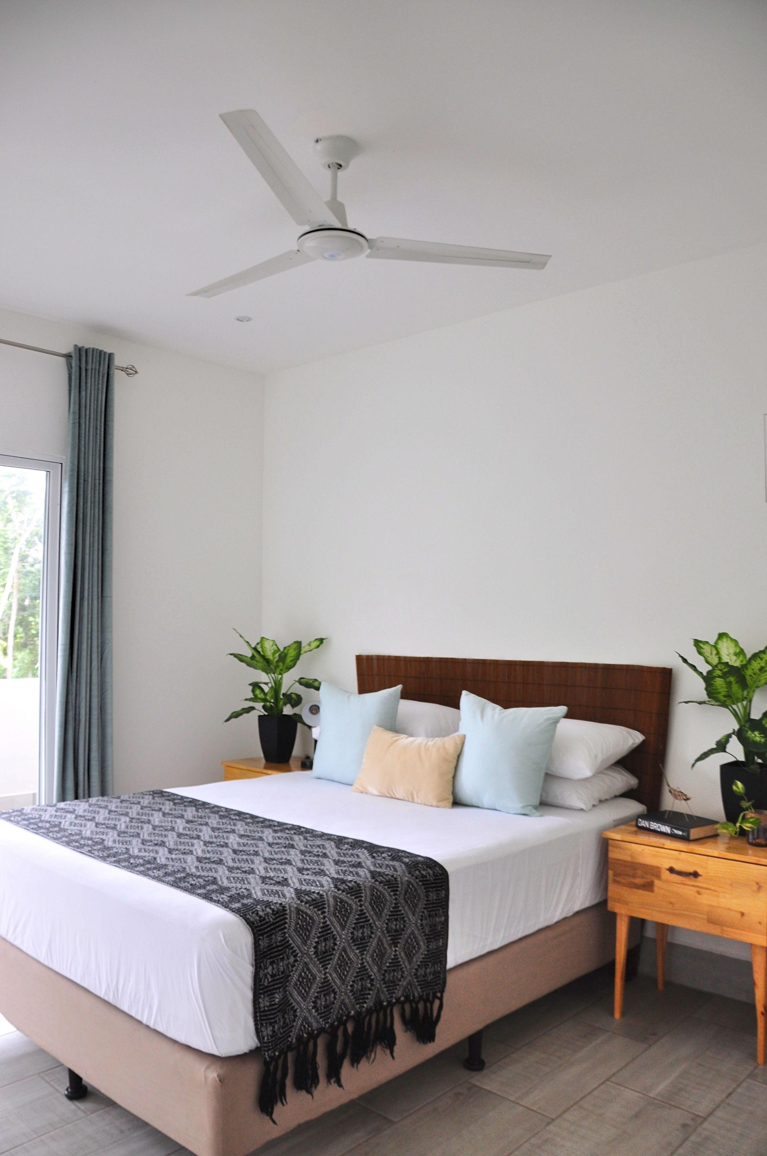Une chambre à coucher avec un lit, des tables de chevet, un ventilateur de plafond et des plantes en pot.