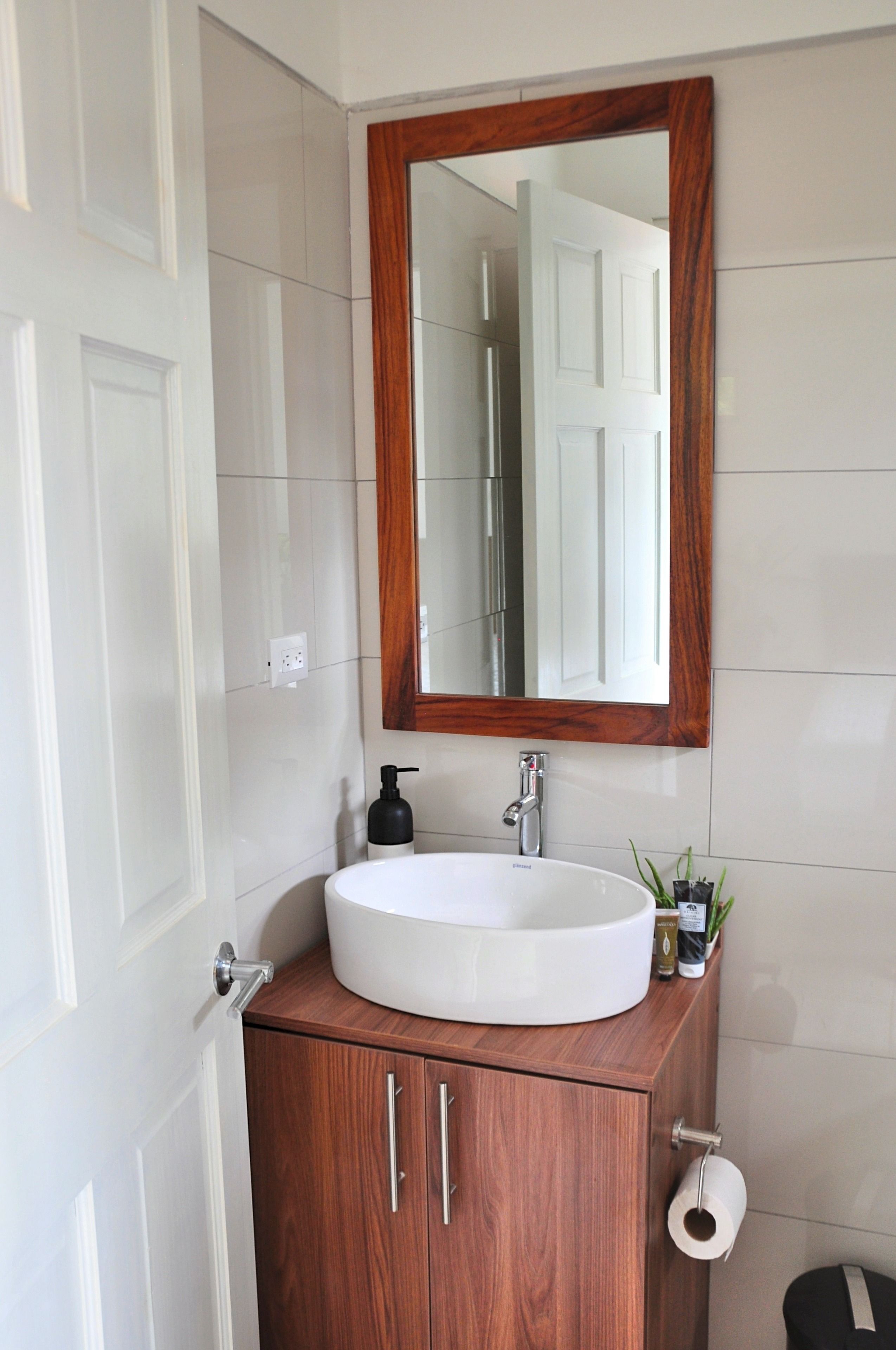 Un bagno con un lavandino bianco, un mobile contenitore in legno e uno specchio con cornice in legno.