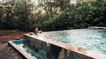 Una piscina rectangular amb una persona relaxant-se al seu interior, envoltada de vegetació abundant.