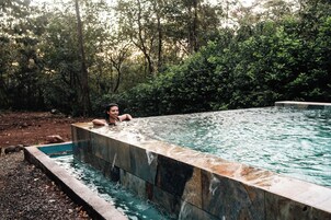 Piscina rectangular con una persona relajándose, rodeada de abundante vegetación.