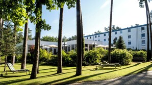 A hotel courtyard with lounge chairs, a paved walkway, and a building with multiple windows. - Heidehotel Bad Bevensen (Bad Bevensen)
