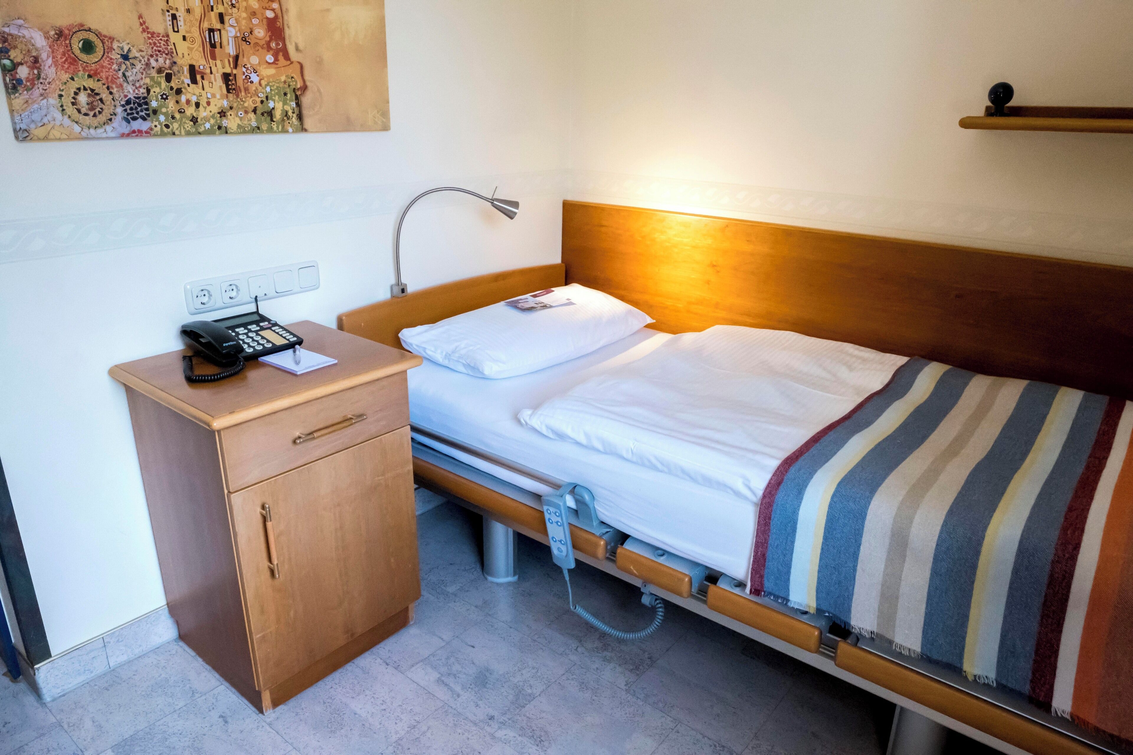 A single bed with a wooden headboard, a bedside table with a lamp, and a telephone.