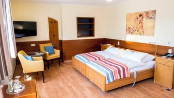 Habitación de hotel con cama, mesita de noche, silla, escritorio, televisor, obras de arte y armario de madera.