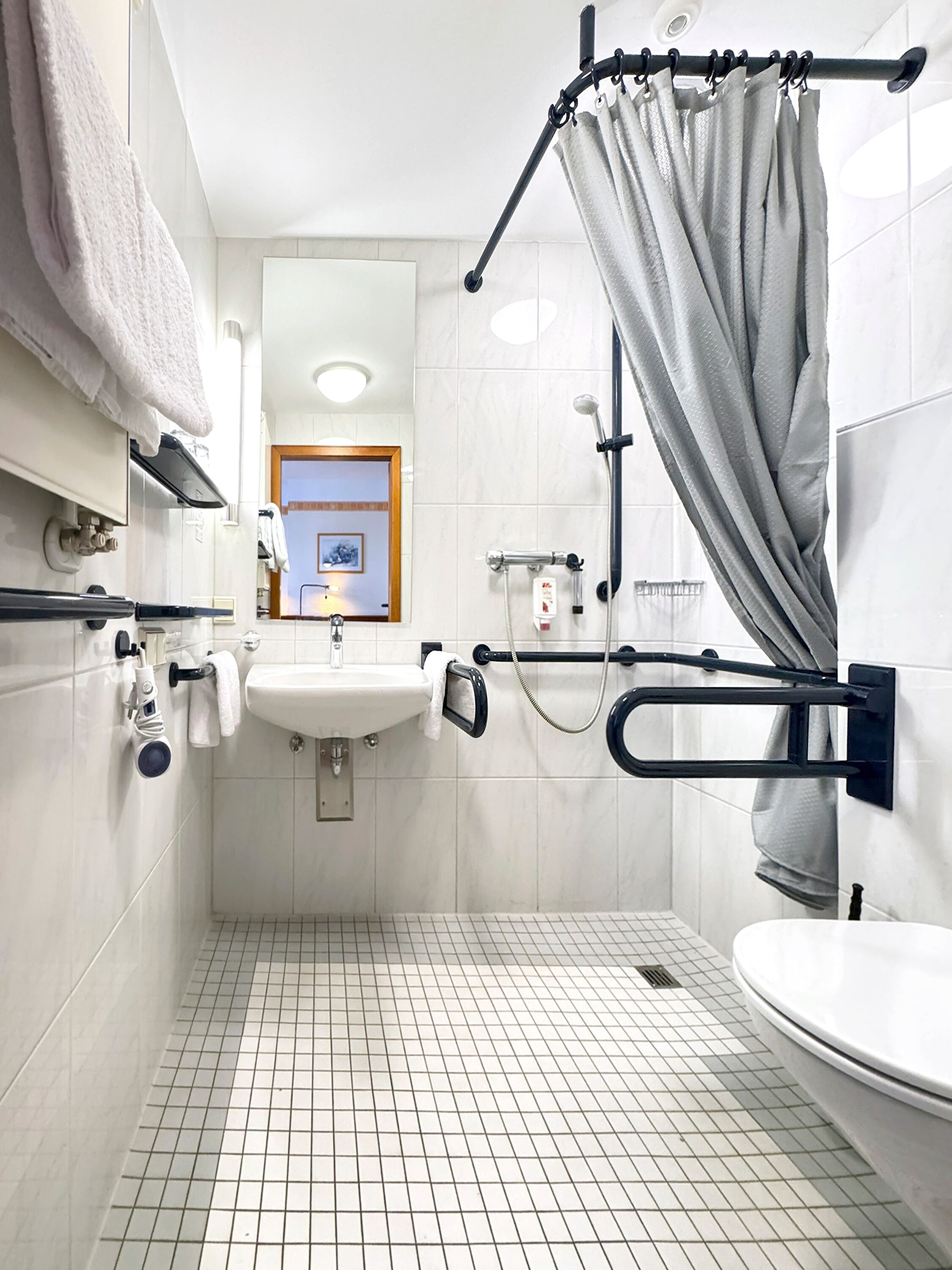 Une salle de bain avec un lavabo blanc, des toilettes, une douche avec un rideau et un porte-serviettes.