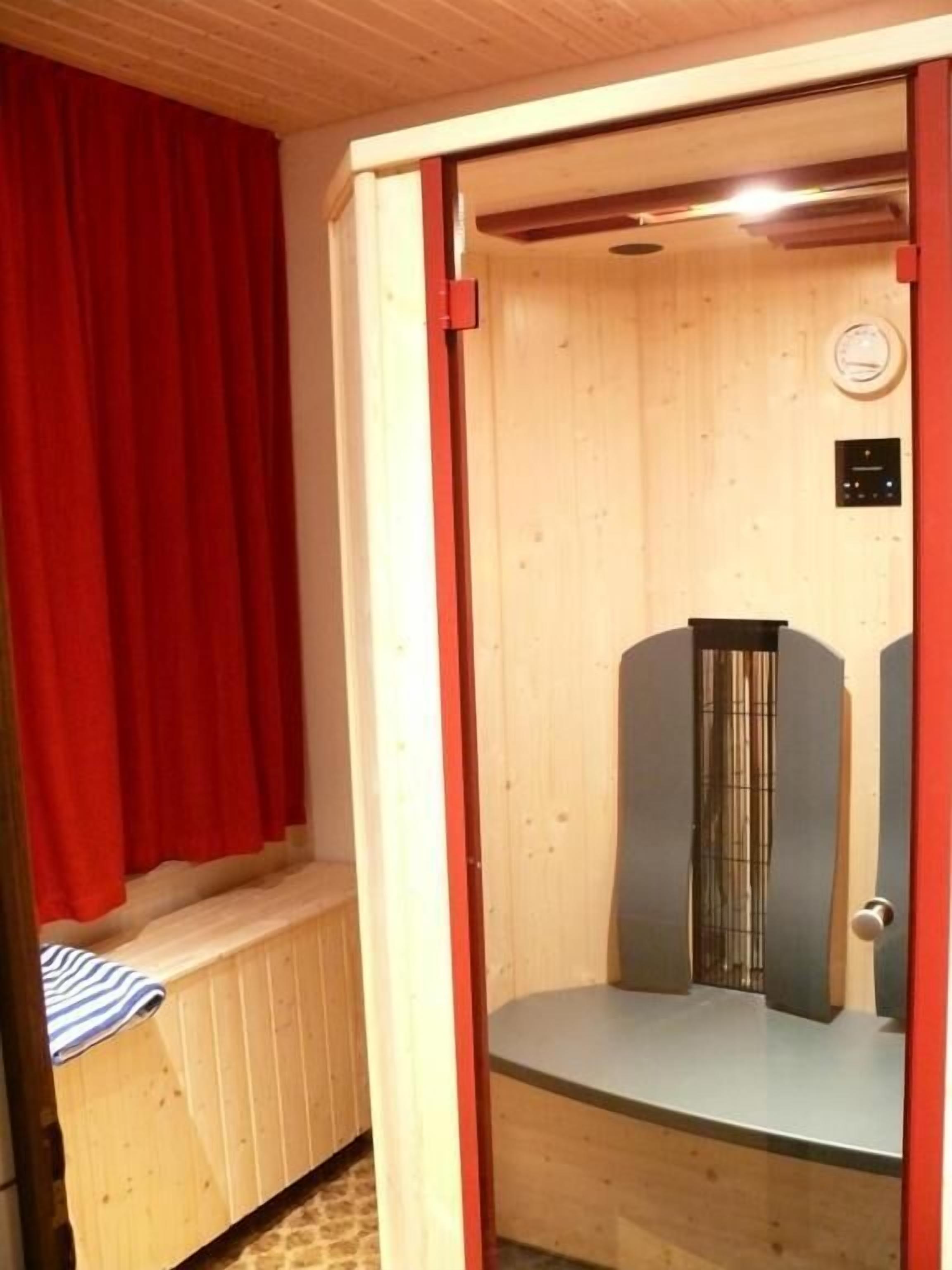A sauna room with a wooden bench, a control panel, and a red curtain.