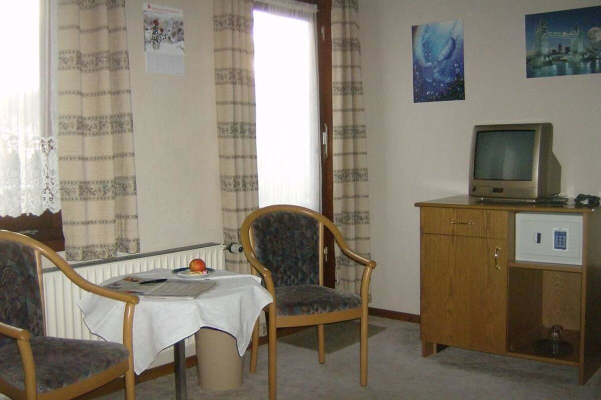 A room with a dining table, two chairs, a television on a wooden cabinet, and a window with curtains.