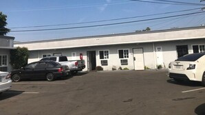 A parking lot with several cars parked in front of a building with a flat roof and a single door. - El Grande Motel (South Gate)