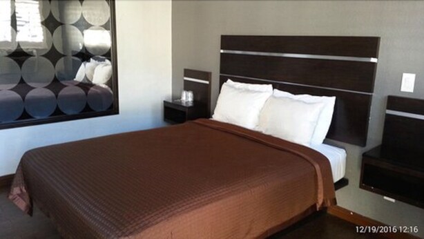 A modern bedroom with a large bed, a headboard with horizontal lines, a nightstand with a lamp, and a wall with circular mirrors. - El Grande Motel (South Gate)