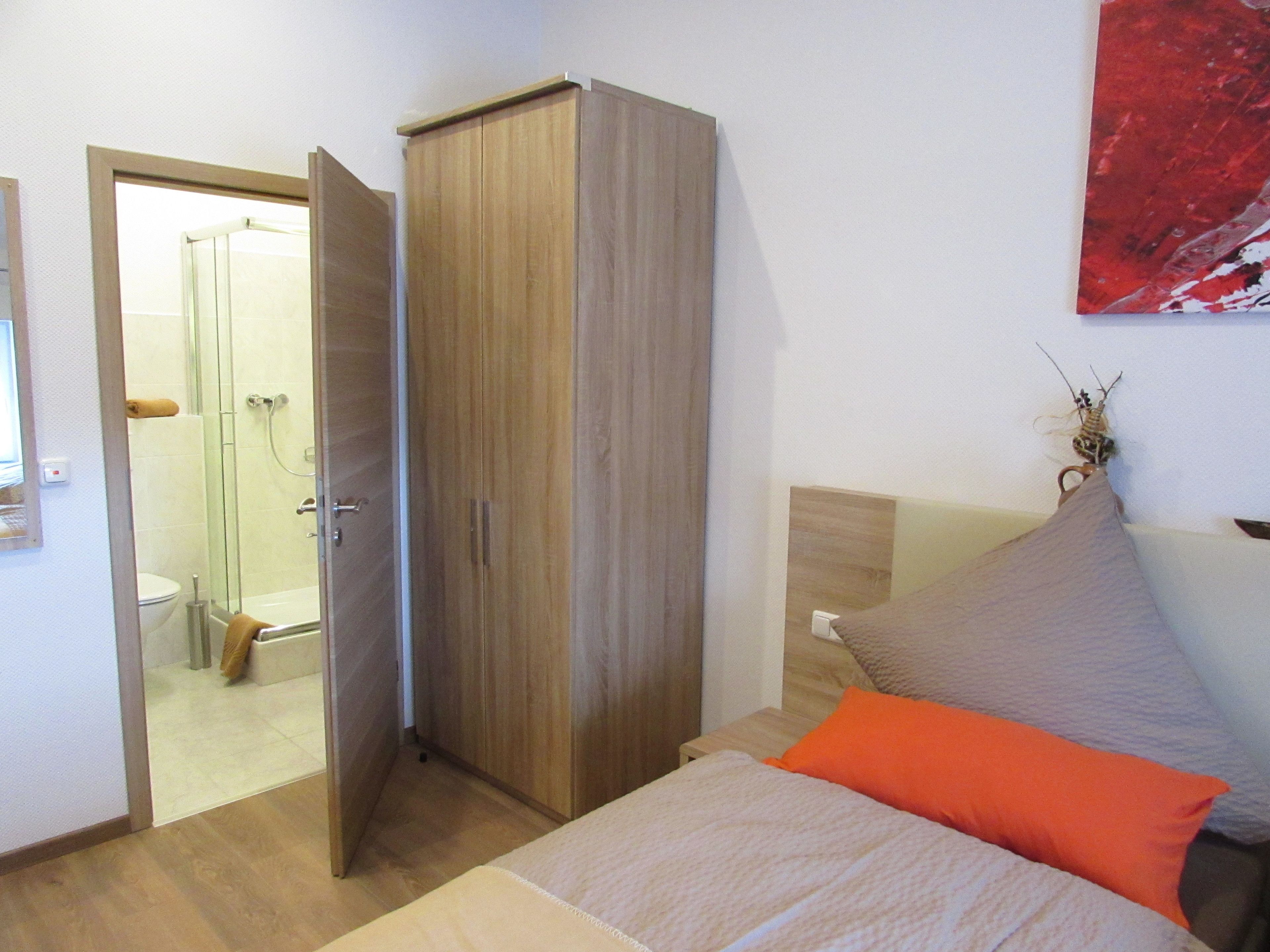 A bedroom with a bed, a wardrobe, and a shower area.