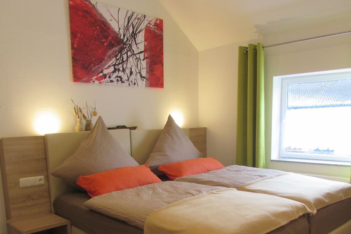 A modern bedroom with a large bed, bedside tables, a nightstand, and a window with curtains.