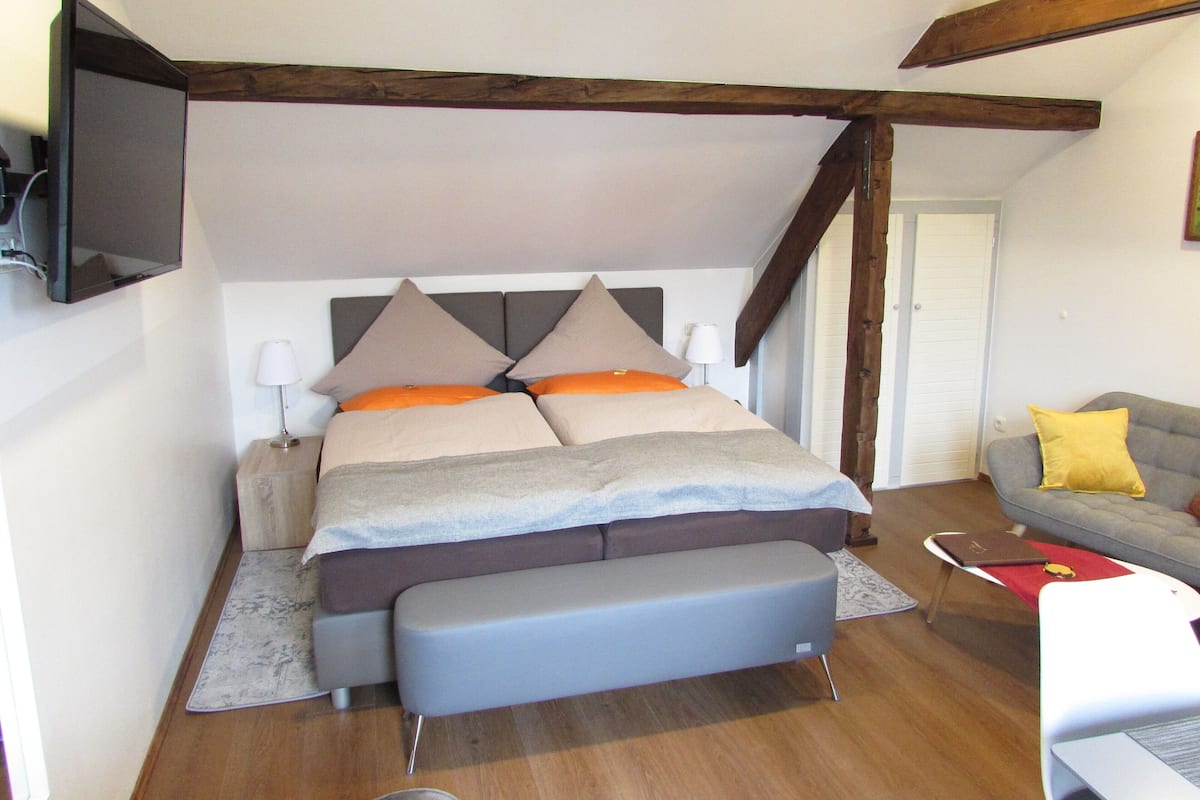 A bedroom with a bed, bench, bedside tables, a flat-screen TV, and a sofa.