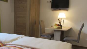 Habitación de hotel con cama, escritorio con lámpara, dos sillas, televisor en la pared y armario.