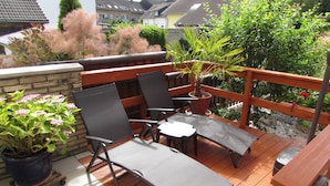 An outdoor deck with two lounge chairs and a table, surrounded by potted plants and a wooden railing. - Eifel Quartier Em Garstüffje (Mechernich)