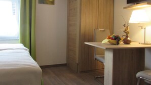 A hotel room with a bed, a desk with a lamp, a television, and a window with curtains. - Eifel Quartier Em Garstüffje (Mechernich)