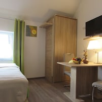 Una habitación de hotel con cama, escritorio con lámpara, televisión y ventana con cortinas.