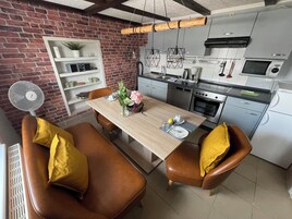 Cocina moderna con pared de ladrillo, techo de madera y electrodomésticos de acero inoxidable. Cuenta con un comedor con mesa de madera y sillas de cuero.