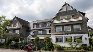 Een gebouw met twee verdiepingen, inclusief een balkon op de bovenverdieping, een kleine winkel met een groene luifel, en een rode motorfiets die ervoor geparkeerd staat.