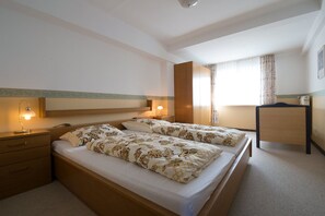 A double bed with floral bedding, a bedside table with a lamp, a wardrobe, and a window with curtains. - Kleines Hotel Wemhoff (Winterberg)