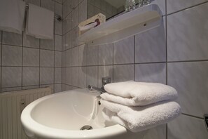 A bathroom with a white sink, a mirror, and a towel rack with folded towels. - Kleines Hotel Wemhoff (Winterberg)