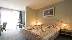 Een hotelkamer met een groot bed, twee nachtkastjes met lampen, een bureau met stoel, een raam met gordijnen en een schilderij aan de muur.