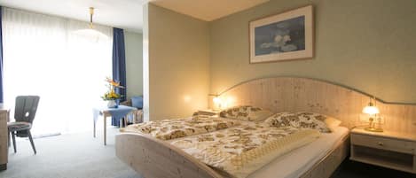 Quarto de hotel com uma cama grande, duas mesas de cabeceira com luminárias, uma escrivaninha com cadeira, uma janela com cortinas e um quadro na parede.