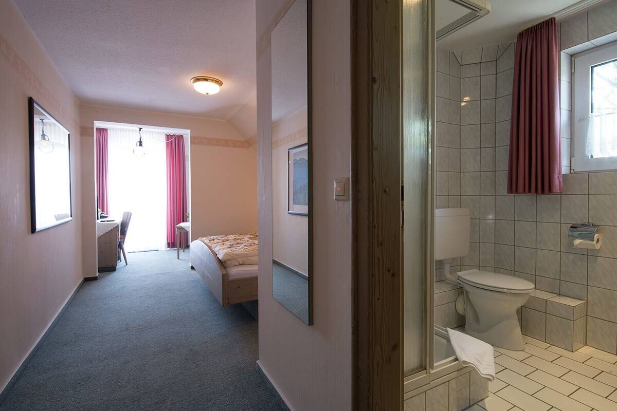 A hotel room with a bed, a desk, a chair, a bathroom with a toilet and a shower.