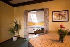 A room with a bed, a dining table, a potted plant, and a kitchen in the background. - Kleines Hotel Wemhoff (Winterberg)