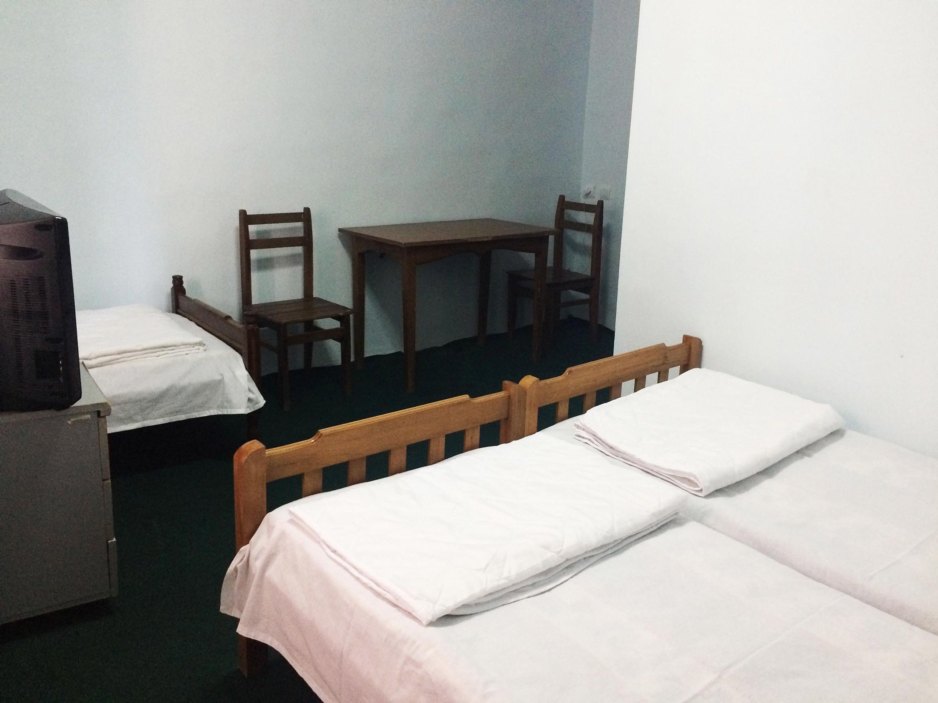 A room with two single beds, a wooden table, two wooden chairs, and a television on a cabinet.