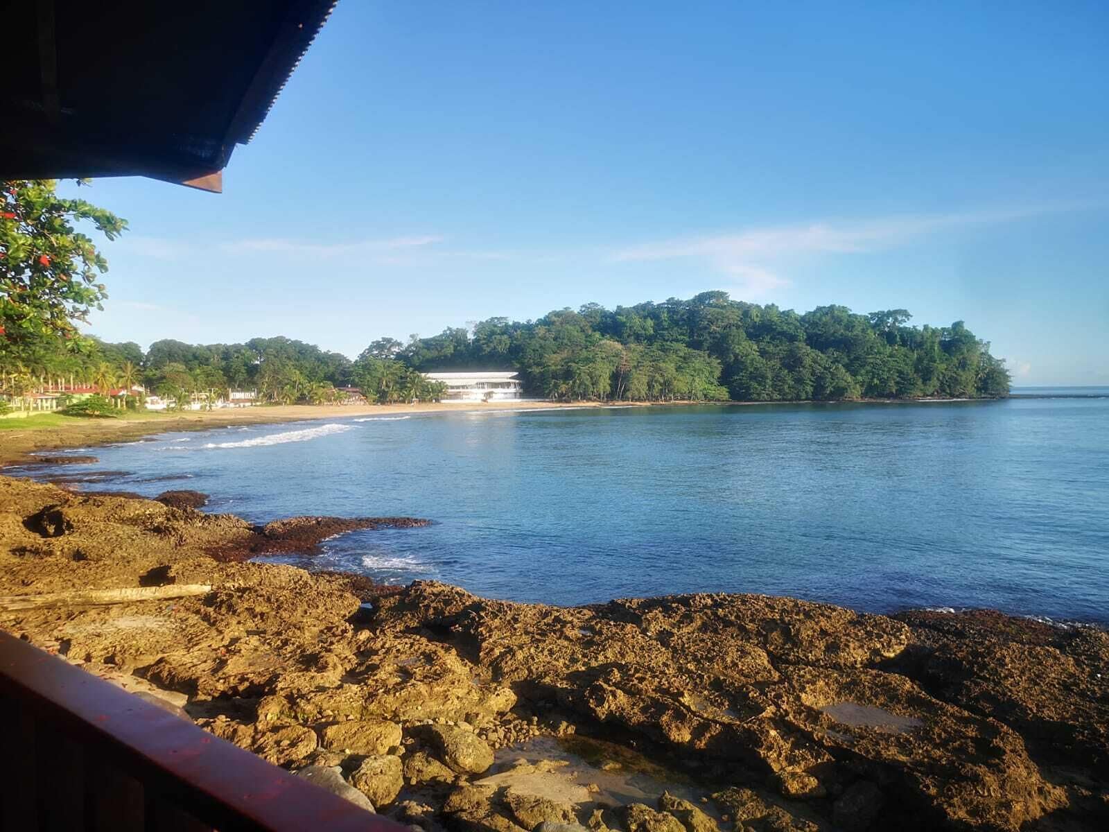 A coastal view with rocky shoreline, a beach, and a building with a white roof on an island.