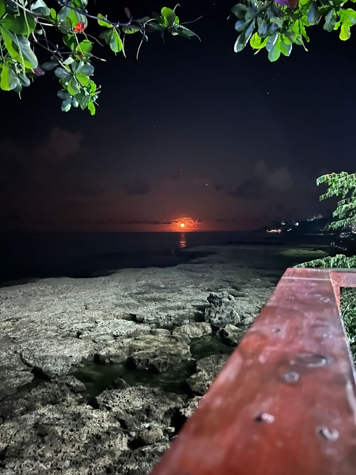 A rocky shoreline at sunset with a wooden bench in the foreground.