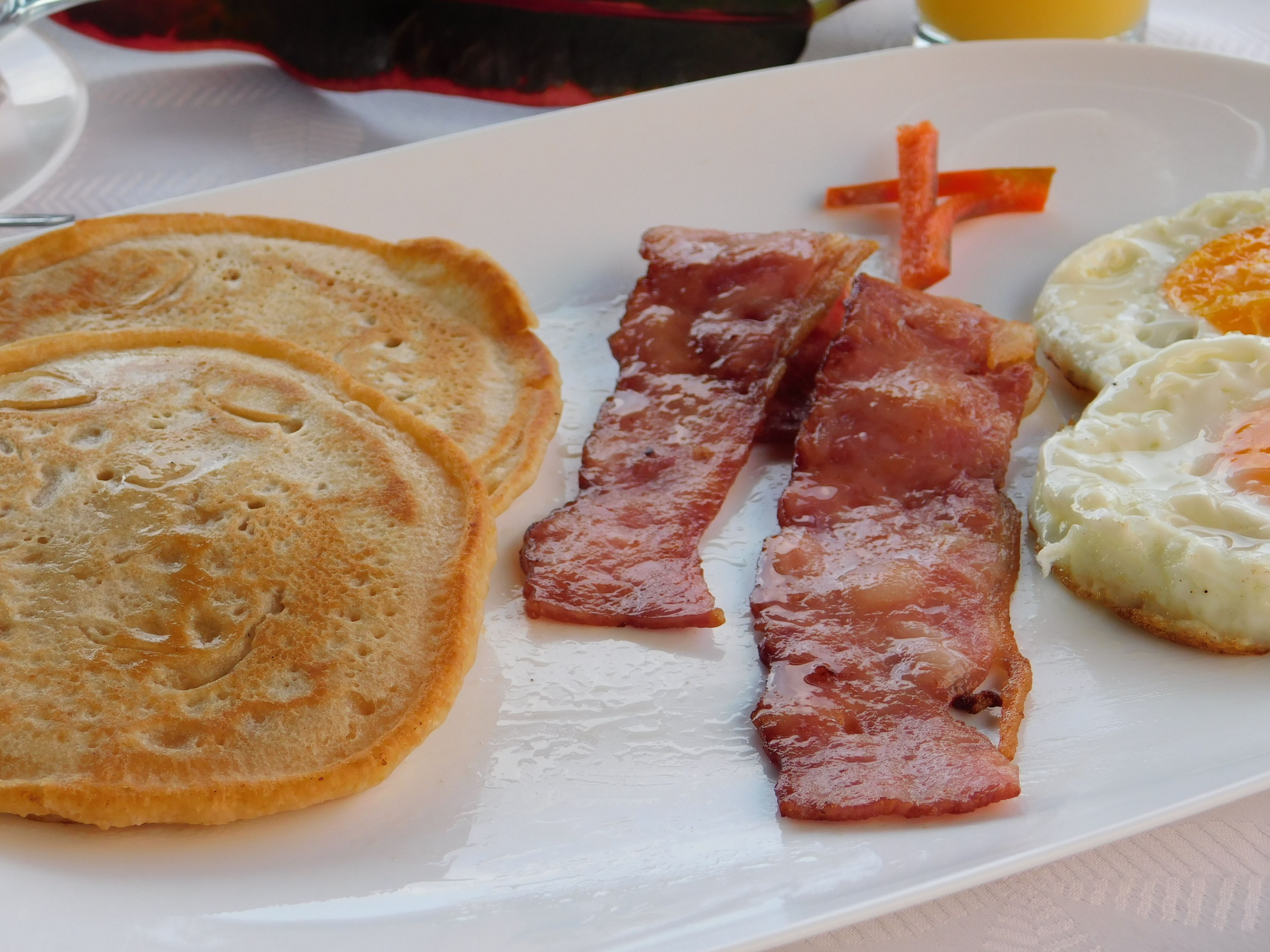 A breakfast plate with pancakes, bacon, and eggs.