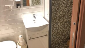 A bathroom with a white sink, a mirror, a toilet, and a shower area with mosaic tiles. - Rent Rooms Colosseum (Rome)