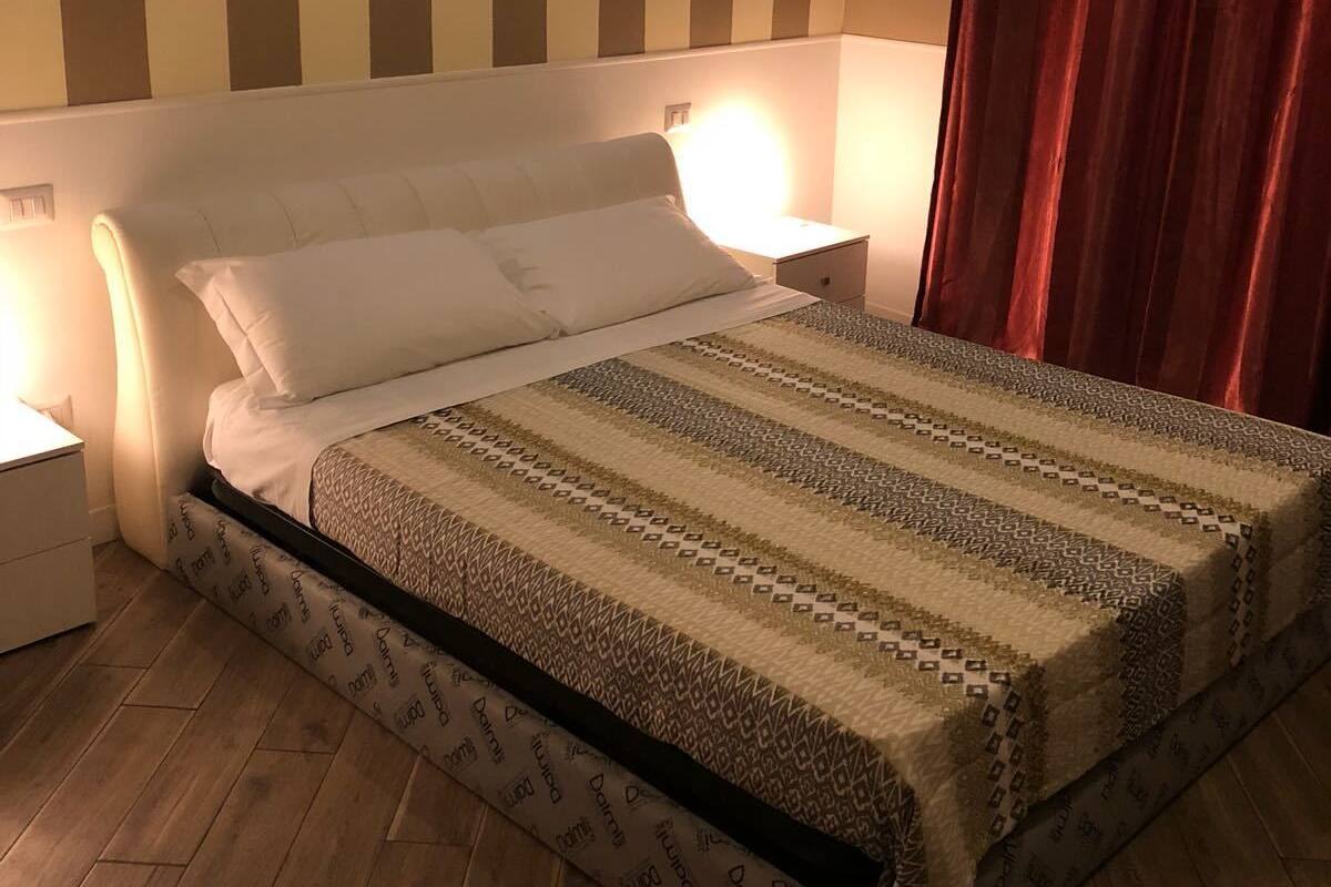 A neatly made bed with a patterned bedspread, a bedside lamp, and a wooden floor.