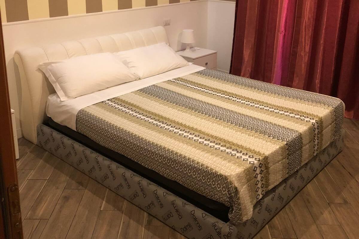A neatly made bed with a patterned bedspread, a bedside table with a lamp, and a striped wall.