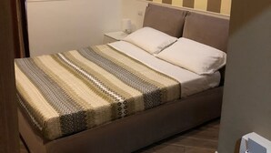 A bedroom with a bed, a bedside table, and a wall with vertical stripes. - Rent Rooms Colosseum (Rome)
