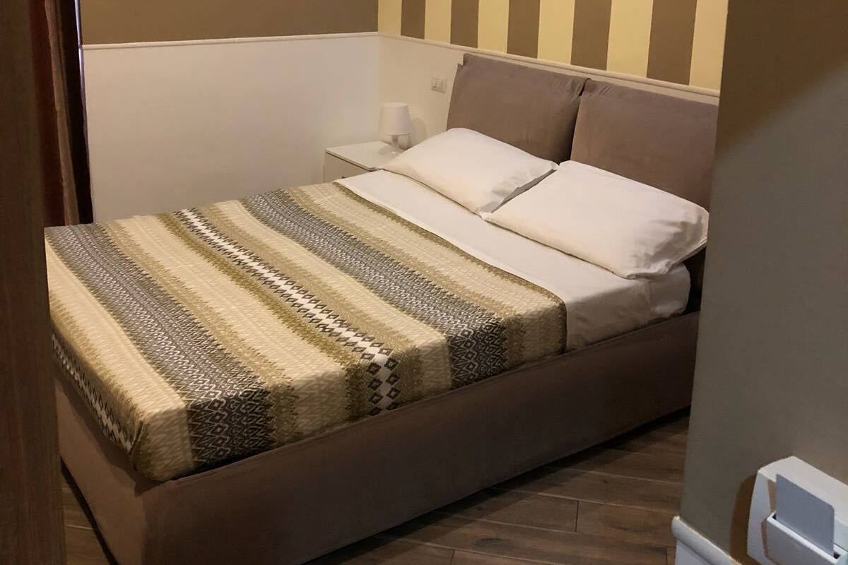 A bedroom with a bed, a bedside table, and a wall with vertical stripes.
