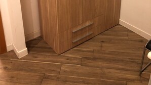 A wooden wardrobe with two doors and a lower shelf, located in a corner of a room with wooden flooring and white walls. - Rent Rooms Colosseum (Rome)